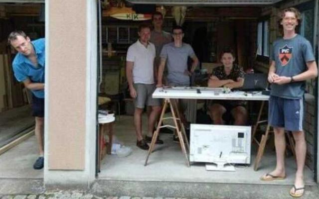 Smiling young men standing in an open garage set up as an office.