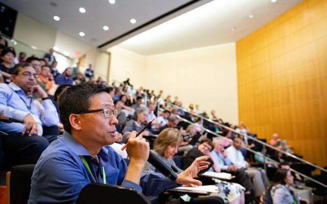 Ben Yu speaking from his seat in a crowded auditorium