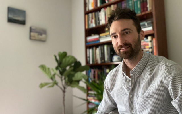 Male graduate student sitting in front of a bookcase