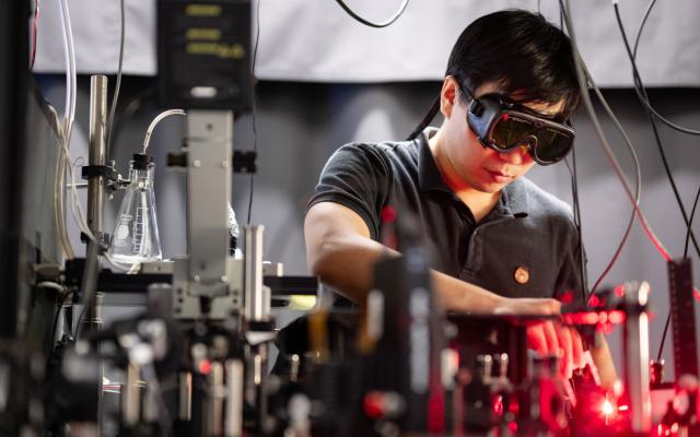 Researcher wearing goggles operates a laser surrounded by lab equipment