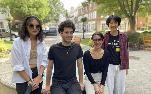 Four smiling young people sitting by a fountain