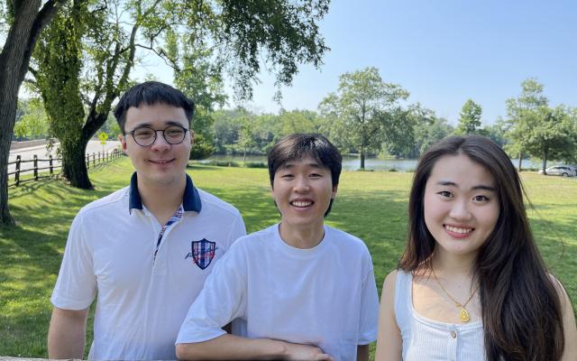 Three students smiling standing in front of Lake Carnegie