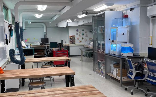 Long room with wood tables and a bank of 3D printers