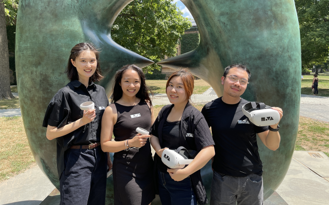 Four students standing in front of a statue holding VR headsets