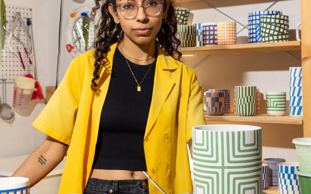 Sarah Hussaini standing at a table surrounded by her pottery. 